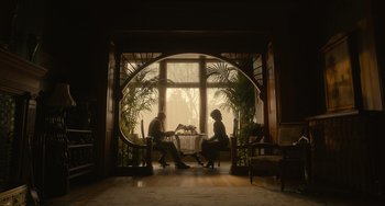 Movie still from “Nightmare Alley” (2021), directed by Guillermo del Toro – Two people sitting at a table in front of an open window; Wide shot, Low angle