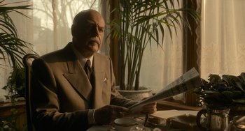 Movie still from “Nightmare Alley” (2021), directed by Guillermo del Toro – An older man sitting at a table reading a newspaper; Medium shot, Low angle
