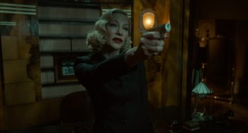 Movie still from “Nightmare Alley” (2021), directed by Guillermo del Toro – A woman holding a gun in a room; Medium shot, Over the shoulder angle