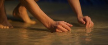 Movie still from “Nine Days” (2020), directed by Edson Oda – A hand is touching the water on the ground; Extreme Close Up shot, High angle