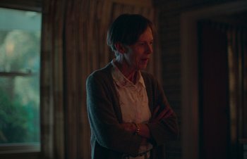 Movie still from “Nitram” (2021), directed by Justin Kurzel – An older woman standing with her arms crossed in a room; Medium shot, Over the shoulder angle