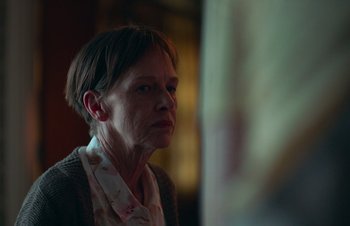 Movie still from “Nitram” (2021), directed by Justin Kurzel – An older woman is looking into the distance; Close Up shot, Over the shoulder angle