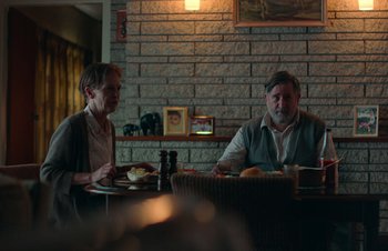 Movie still from “Nitram” (2021), directed by Justin Kurzel – A man and a woman are sitting at a table; Medium shot, Over the shoulder angle