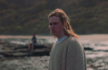 Movie still from “Nitram” (2021), directed by Justin Kurzel – A man with long blonde hair standing in the water; Close Up shot, Low angle