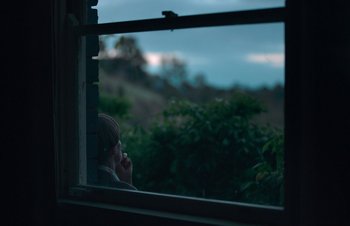 Movie still from “Nitram” (2021), directed by Justin Kurzel – A person is looking out of a window at dusk; Medium shot, Over the shoulder angle