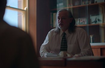 Movie still from “Nitram” (2021), directed by Justin Kurzel – A man sitting at a table in front of a window; Medium shot, Over the shoulder angle