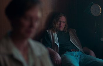 Movie still from “Nitram” (2021), directed by Justin Kurzel – A man sitting on a couch next to another man; Medium shot, High angle