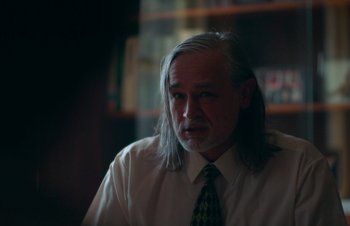Movie still from “Nitram” (2021), directed by Justin Kurzel – A man with long grey hair wearing a white shirt; Close Up shot, Over the shoulder angle