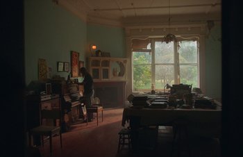 Movie still from “Nitram” (2021), directed by Justin Kurzel – A person is playing piano in a living room; Wide shot, High angle