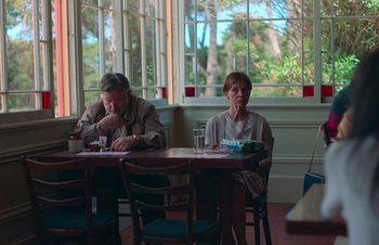 Movie still from “Nitram” (2021), directed by Justin Kurzel – A man and a woman sitting at a table in front of a window; Medium shot, Low angle