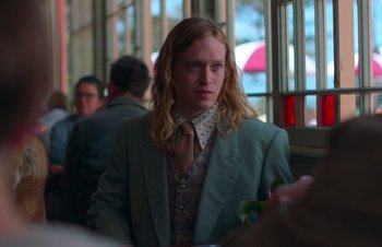 Movie still from “Nitram” (2021), directed by Justin Kurzel – A man with long blonde hair wearing a suit and tie; Medium shot, Over the shoulder angle