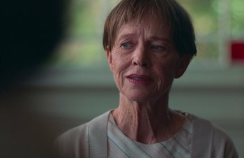 Movie still from “Nitram” (2021), directed by Justin Kurzel – An older woman with short brown hair wearing a white shirt; Close Up shot, Over the shoulder angle