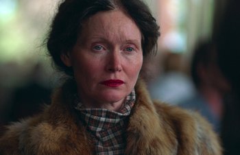 Movie still from “Nitram” (2021), directed by Justin Kurzel – An older woman wearing a plaid shirt and a fur coat; Close Up shot, Over the shoulder angle