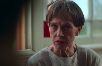 Movie still from “Nitram” (2021), directed by Justin Kurzel – An older woman with short brown hair looking at the camera; Close Up shot, Low angle