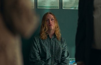 Movie still from “Nitram” (2021), directed by Justin Kurzel – A man with long blonde hair sitting in front of a mirror; Medium shot, Over the shoulder angle