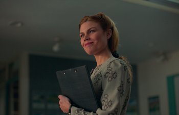 Movie still from “Nitram” (2021), directed by Justin Kurzel – A woman is holding a folder and smiling for the camera; Close Up shot, Low angle