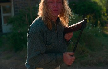 Movie still from “Nitram” (2021), directed by Justin Kurzel – A person holding a gun in a field; Medium shot, High angle