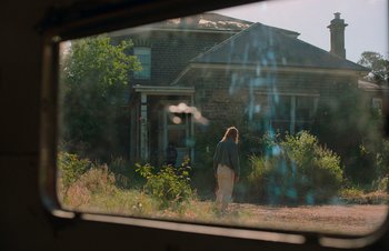 Movie still from “Nitram” (2021), directed by Justin Kurzel – A woman walking down a dirt road in front of a house; Wide shot, Over the shoulder angle