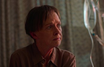 Movie still from “Nitram” (2021), directed by Justin Kurzel – An older woman with short brown hair looking off into the distance; Close Up shot, Over the shoulder angle