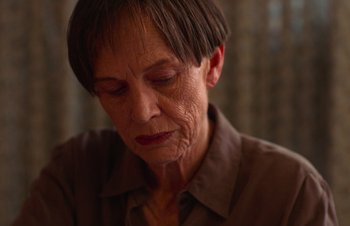 Movie still from “Nitram” (2021), directed by Justin Kurzel – An older woman with short hair is looking down; Close Up shot, High angle