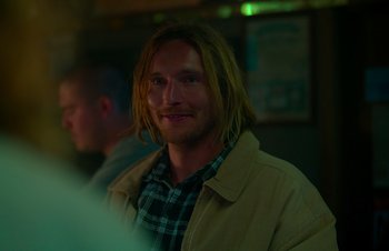 Movie still from “Nitram” (2021), directed by Justin Kurzel – A man with long blonde hair and a plaid shirt; Close Up shot, Over the shoulder angle