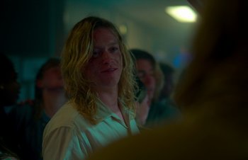 Movie still from “Nitram” (2021), directed by Justin Kurzel – A man with blonde hair is standing in front of a group of people; Close Up shot, Over the shoulder angle