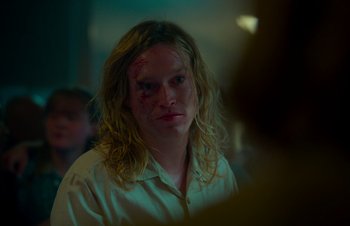 Movie still from “Nitram” (2021), directed by Justin Kurzel – A man with long blonde hair is looking at the camera; Close Up shot, Over the shoulder angle