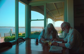 Movie still from “Nitram” (2021), directed by Justin Kurzel – Two people sitting at a table with a view in the background; Medium shot, High angle
