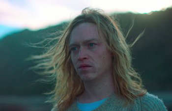 Movie still from “Nitram” (2021), directed by Justin Kurzel – A person with long blonde hair; Close Up shot, Low angle