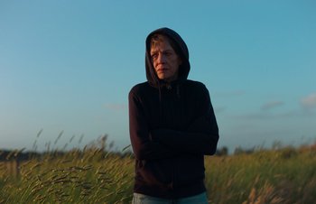Movie still from “Nitram” (2021), directed by Justin Kurzel – A person standing in a field wearing a black hoodie; Medium shot, Low angle