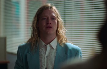 Movie still from “Nitram” (2021), directed by Justin Kurzel – A man with long blonde hair wearing a blue jacket; Medium shot, Over the shoulder angle