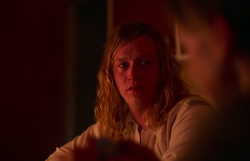 Movie still from “Nitram” (2021), directed by Justin Kurzel – A man with long blonde hair is looking at the camera; Close Up shot, Over the shoulder angle