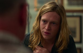 Movie still from “Nitram” (2021), directed by Justin Kurzel – A man with long blonde hair is looking at the camera; Close Up shot, Over the shoulder angle