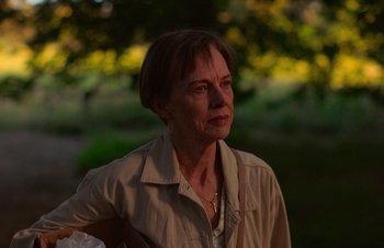 Movie still from “Nitram” (2021), directed by Justin Kurzel – An older woman in a tan shirt is looking at the camera; Close Up shot, Over the shoulder angle