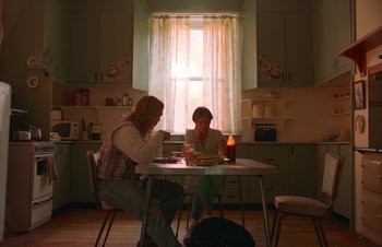 Movie still from “Nitram” (2021), directed by Justin Kurzel – Two people sitting at a table in a kitchen; Medium shot, Low angle