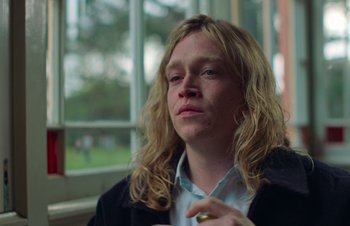 Movie still from “Nitram” (2021), directed by Justin Kurzel – A man with long blonde hair is sitting in front of a window; Close Up shot, Low angle