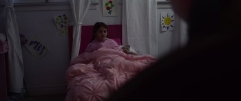 Movie still from “Nix” (2022), directed by Anthony C. Ferrante – A little girl laying in a bed with a teddy bear; Medium shot, High angle