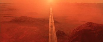 Movie still from “No Escape” (1994), directed by Martin Campbell – An aerial view of an empty road in the middle of the desert; Extreme Wide shot, High angle