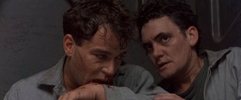 Movie still from “No Escape” (1994), directed by Martin Campbell – Two men are looking at each other with blood on their face; Close Up shot, Low angle
