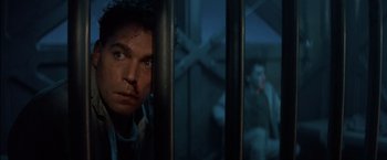 Movie still from “No Escape” (1994), directed by Martin Campbell – A person behind a fence; Close Up shot, Low angle