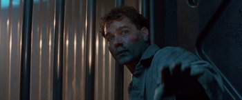 Movie still from “No Escape” (1994), directed by Martin Campbell – A person wearing a shirt with blue paint on his face; Close Up shot, Low angle