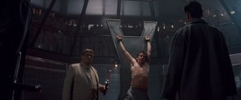 Movie still from “No Escape” (1994), directed by Martin Campbell – A man is holding a sword in a room; Medium shot, Low angle