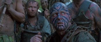 Movie still from “No Escape” (1994), directed by Martin Campbell – A man with blue and black face paint and blue eyes; Close Up shot, Low angle