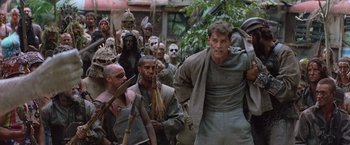 Movie still from “No Escape” (1994), directed by Martin Campbell – A group of men standing next to each other in front of a building; Medium shot, Low angle