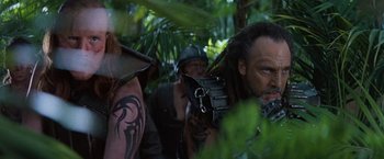 Movie still from “No Escape” (1994), directed by Martin Campbell – A group of people in the woods with tattoos on their faces; Close Up shot, Low angle
