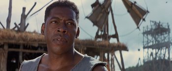 Movie still from “No Escape” (1994), directed by Martin Campbell – A person with a boat in the background; Close Up shot, Low angle