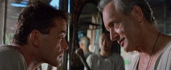 Movie still from “No Escape” (1994), directed by Martin Campbell – A group of men standing next to each other in a room; Close Up shot, Over the shoulder angle