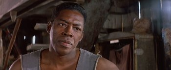Movie still from “No Escape” (1994), directed by Martin Campbell – A person wearing a tank top; Close Up shot, Low angle