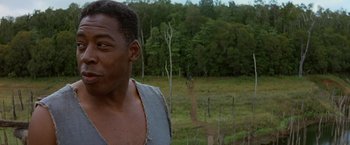 Movie still from “No Escape” (1994), directed by Martin Campbell – A man standing in front of a forest with trees in the background; Close Up shot, Over the shoulder angle