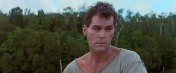 Movie still from “No Escape” (1994), directed by Martin Campbell – A person wearing a shirt with trees in the background; Close Up shot, Low angle